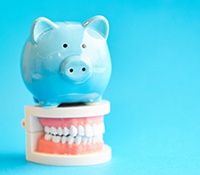 blue piggy bank and model teeth symbolizing cost of dental implants in Allen