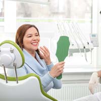 Middle-aged woman admiring her new prosthetic teeth in mirror