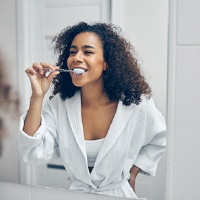 Woman in white robe brushing teeth in front of mirror