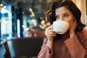 Woman with dark hair and veneers enjoying a cup of coffee