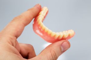 Hand holding lower denture against neutral background